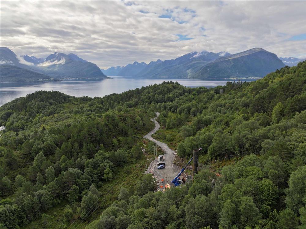 grøn natur med anleggsveg, blå fjord og fjell i bakgrunnen - Klikk for stort bilete